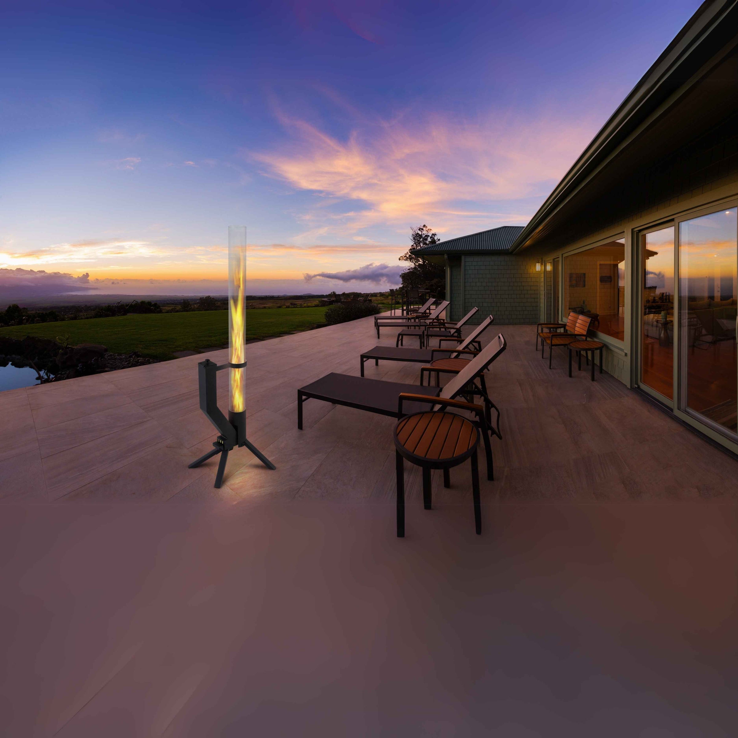 GardenFlare Feuerrohr auf einer modernen Terrasse mit Liegestühlen bei Sonnenuntergang, mit Blick auf eine weite Landschaft und einen farbenfrohen Himmel.