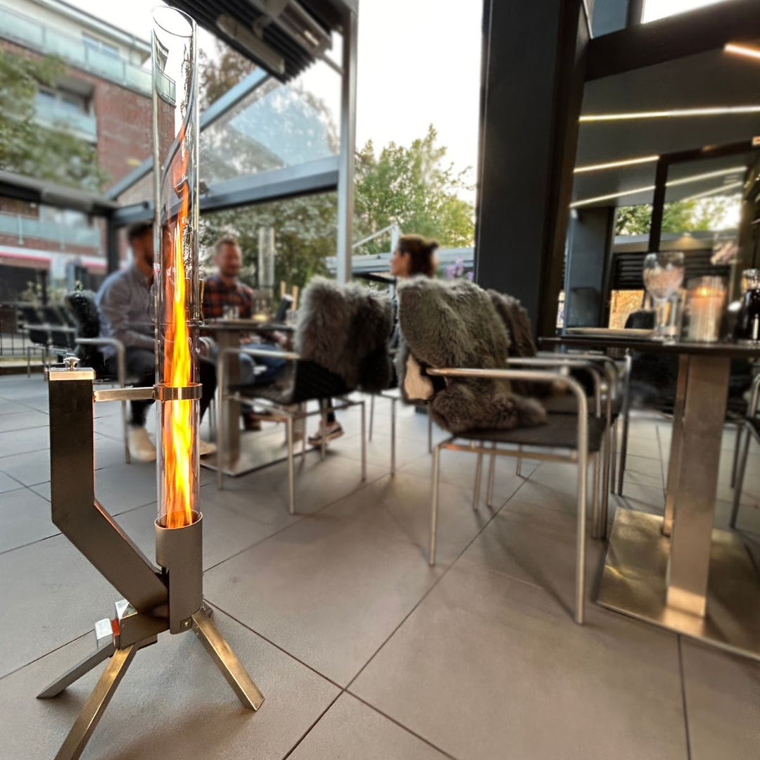 Klassik Feuerrohr Silber auf einer modernen Terrasse mit sichtbarer Flamme und gemütlicher Atmosphäre am Abend.
