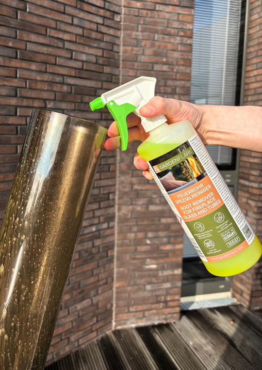 Hand sprüht mit Gardenflare Feuerrohr-Spezialreiniger auf ein verrußtes Glasrohr, um Ruß und Schmutz zu entfernen.