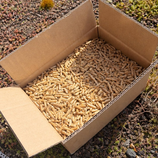 Offene Kartonbox mit Gardenflare Premium Holzpellets 3,5 kg im Außenbereich auf Naturboden, Brennstoff für pelletbetriebene Feuerstellen