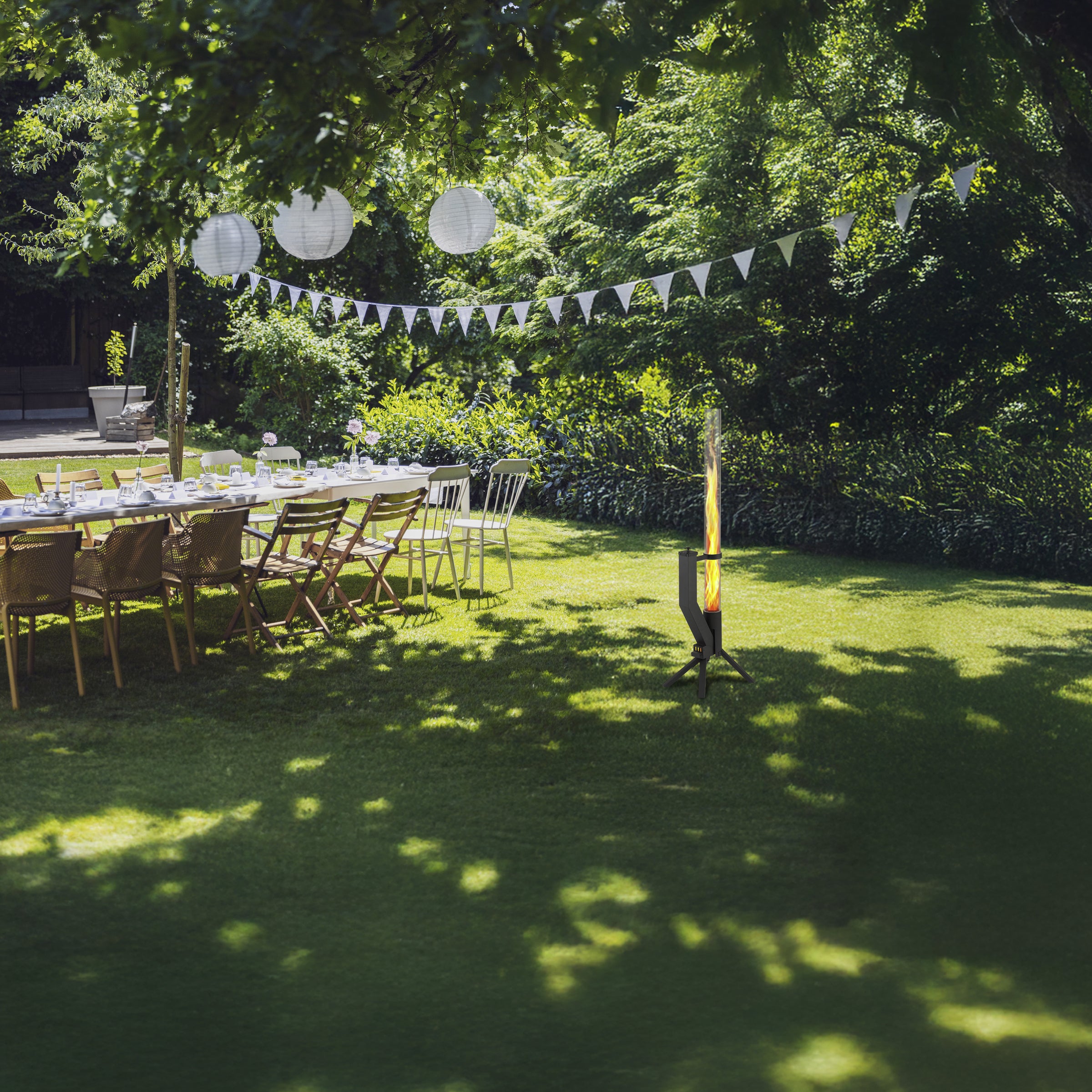 Gartenfeier mit gedeckter Tafel unter Bäumen und brennendem Gardenflare Premium Feuerrohr in Schwarz im Vordergrund.