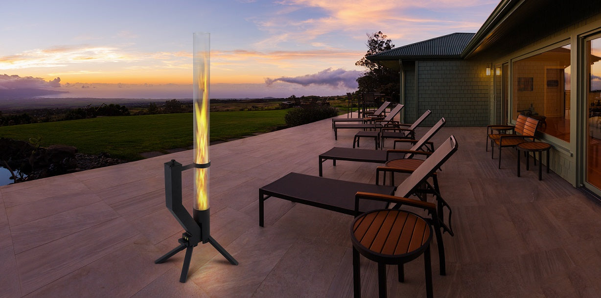 Moderne Terrasse bei Sonnenuntergang mit einem schwarzen Feuerrohr als stimmungsvolle Beleuchtung, umgeben von Liegestühlen und einem weiten Blick ins Grüne.
